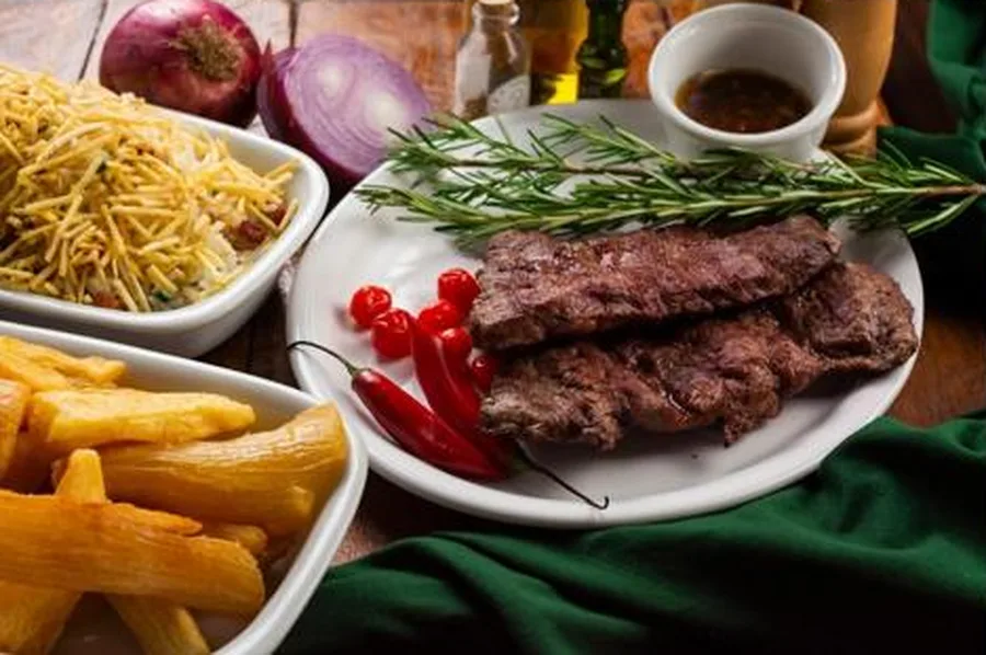 Fatias de carne grelhada com alecrim, batata palha e mandioca frita