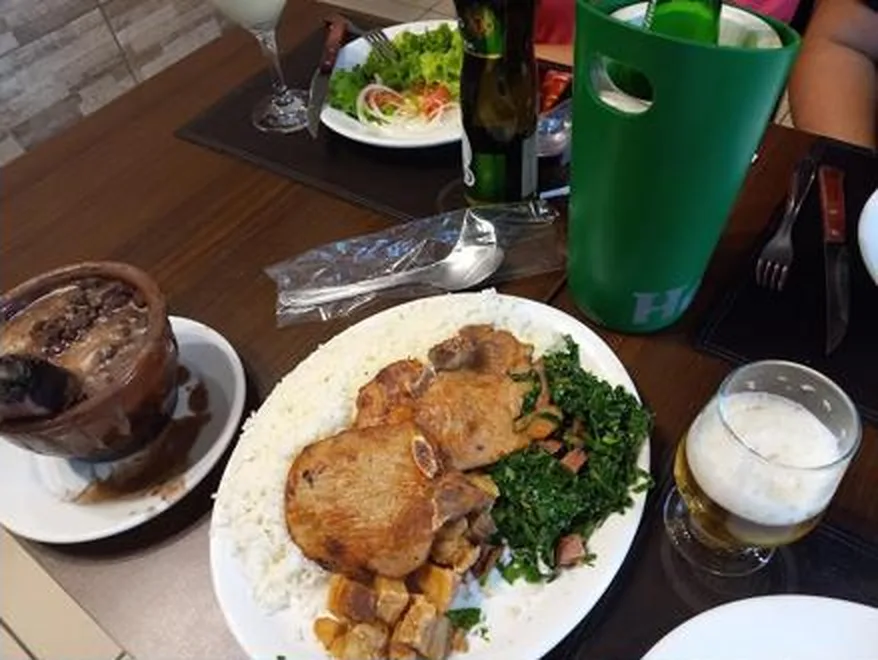 Prato com arroz, couve, carne e torresmo ao lado de cumbuca de feijão e copo de chope